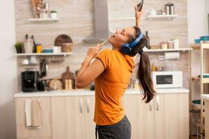 vrolijk vrouw het zingen in de keuken in de ochtend. energiek, positief, Vrolijk, grappig en schattig huisvrouw dansen alleen in de huis. vermaak en vrij alleen Bij huis foto