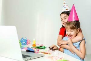 kinderen online verjaardag feest. weinig meisjes in jurken, hoed vieren vakantie met vrienden. conferentie, filmpje telefoontje in laptop, computer. quarantaine, coronavirus pandemisch covid19. foto