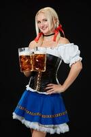 jong sexy vrouw vervelend een dirndl met twee bier mokken Aan zwart achtergrond. foto