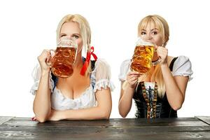 twee mooi Dames drinken bier van groot bril terwijl zittend Bij een houten tafel Aan een wit achtergrond in de studio foto