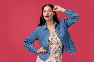 portret van een mooi jong vrouw in een licht jurk en blauw overhemd staand Aan roze achtergrond in studio. mensen oprecht emoties. foto