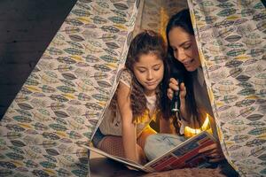 moeder en dochter zijn zittend in een Tipi tent, lezing verhalen met de zaklamp. gelukkig familie. foto