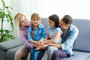 vrolijk jong familie met kinderen lachend zittend Aan bankstel samen, ouders met kinderen genieten van onderhoudend Bij huis foto