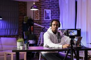 vlogger opname internet tonen gebruik makend van modern camera, pratend over Internationale nieuws en evenementen onderwerpen. Mens filmen leven uitzending gebruik makend van professioneel gadgets in rgb lichten studio foto