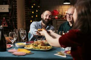 personen aan het eten voedsel Bij feestelijk diner, vieren Kerstmis vooravond samen en voorbijgaan maaltijd borden in de omgeving van. blij groep van mensen genieten van vakantie viering evenement Bij huis, winter feest. foto