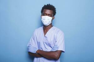 portret van zwart Mens vervelend gezicht masker en uniform staand in studio, werken voor gezondheidszorg. medisch assistent op zoek Bij camera, hebben bescherming tegen coronavirus. foto