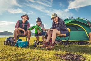 groep reizigers kamperen en picknicken in de weide met tent voorgrond. berg en meer achtergrond. mensen en levensstijlen concept. buitenshuis activiteit en vrije tijd thema. backpacker en wandelaar thema foto