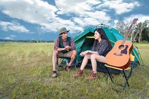 twee mensen praten in de buurt van camping tent in weide veld. mannelijke en vrouwelijke reiziger die naar het gezichtspunt van de attractie kijken. paren avontuur in de buitenlucht samen. mensen en levensstijlen concept foto