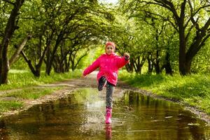 gelukkig kind meisje met rubber laarzen in plas Aan een herfst wandelen foto