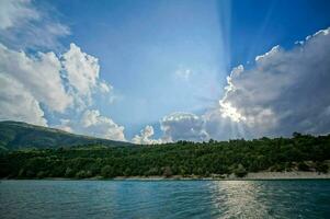 de zon schijnt door wolken over- een meer foto