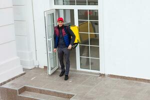 portret van een vrolijk levering Mens staand met geel thermo rugzak voor voedsel levering Aan de straat buitenshuis foto