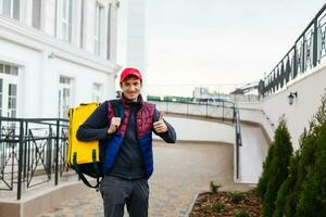 portret van een vrolijk levering Mens staand met geel thermo rugzak voor voedsel levering Aan de straat buitenshuis foto