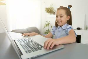 vrolijk schattig meisje kinderen opgewonden gebruik makend van computer aan het leren school werk. kind genieten e-learning in vakantie Bij huis. foto