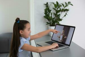 vrolijk schattig meisje kinderen opgewonden gebruik makend van computer aan het leren school werk. kind genieten e-learning in vakantie Bij huis. foto