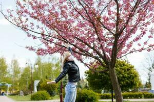 gelukkig jong vrouw vervelend gelaats masker voor virus bescherming staand buitenshuis Aan zonnig voorjaar dag. foto