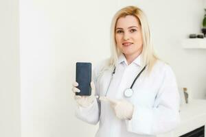 portret van vrouw dokter gebruik makend van haar mobiel telefoon in de overleg. foto
