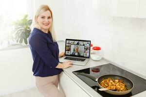 mooi meisje is aan het leren naar koken gezond voedsel online door de internet van een laptop in grijs keuken Aan tafel. foto