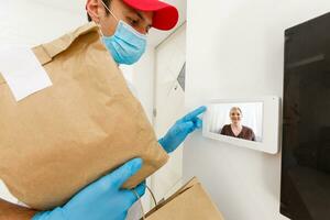 huis levering, online bestellen. een Mens in uniform, een medisch masker en rubber handschoenen met een doos, een pakket in zijn handen. voedsel en voedsel levering gedurende de quarantaine van de coronavirus pandemisch foto