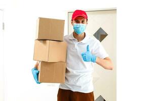 een Mens een medisch masker en blauw rubber handschoenen met een doos, een pakket in zijn handen. voedsel levering gedurende de quarantaine van de coronavirus pandemie. huis levering, online bestellen. online boodschappen doen . foto
