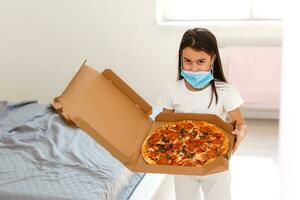 weinig meisje Bij huis gedurende quarantaine en aan het eten pizza. foto