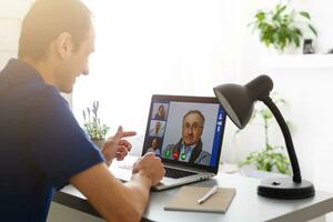 Mens hebben video babbelen met dokter Aan laptop Bij huis foto