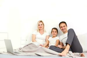 gelukkig familie leugens Aan bed en aan het kijken iets Aan laptop. foto