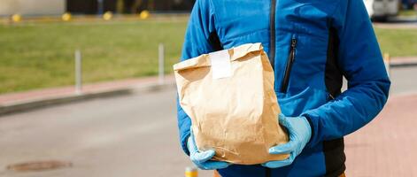 levering Mens Holding papier zak met voedsel, voedsel levering Mens in beschermend masker foto