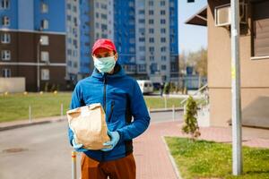 levering Mens Holding papier zak met voedsel, voedsel levering Mens in beschermend masker foto