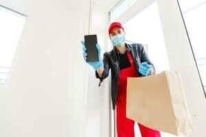 levering Mens in beschermend masker en medisch handschoenen Holding een papier doos. levering onderhoud onder quarantaine, ziekte uitbraak, coronavirus covid-19 pandemisch conditie. foto