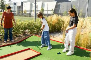 schattig school- meisje spelen mini golf met familie. gelukkig kleuter kind hebben pret met buitenshuis werkzaamheid. zomer sport voor kinderen en volwassenen, buitenshuis. familie vakanties of toevlucht. foto