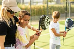 jong sportief vrouw met kinderen spelen padel spel in rechtbank Aan zonnig dag foto