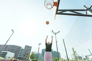 concept van sport, hobby's en gezond levensstijl. jong atletisch meisje is opleiding naar Speel basketbal Aan modern buitenshuis basketbal rechtbank. gelukkig vrouw foto