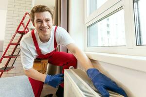 een loodgieter is vaststelling een radiator. met een verstelbaar moersleutel, hij verstrakt de tik. een aktentas met een gereedschap Bij hand- foto