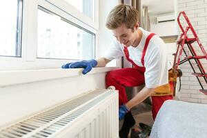 een loodgieter is vaststelling een radiator. met een verstelbaar moersleutel, hij verstrakt de tik. een aktentas met een gereedschap Bij hand- foto