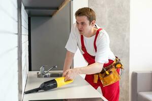 jong knap Mens schoonmaak huis. aantrekkelijk vent Holding vacuüm schoonmaakster in de keuken foto