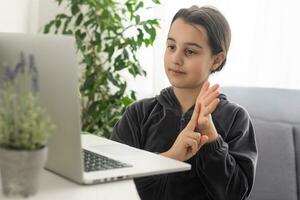 glimlachen tiener- meisje doof gehandicapt kind school- meisje aan het leren online klasse Aan laptop communiceren met leraar door video conferentie telefoontje gebruik makend van teken taal tonen hand- gebaar gedurende virtueel les. foto