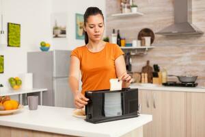 vrouw roosteren brood plakjes Aan elektrisch tosti apparaat voor ontbijt maaltijd. huisvrouw gebruik makend van brood tosti apparaat voor heerlijk ontbijt. gezond ochtend- in knus interieur, heerlijk huis maaltijd voorbereiding. foto