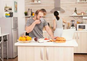freelancer drinken koffie en werken van huis terwijl zijn vrouw bereidt zich voor de ontbijt. freelancer werk online via internet gebruik makend van modern digitaal technologie foto