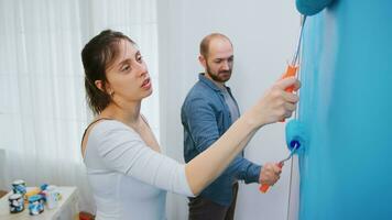 vriendin en vriendje schilderij muur met blauw verf gedurende leven kamer make-over. appartement herinrichting en huis bouw terwijl renoveren en verbeteren. reparatie en decoreren. foto