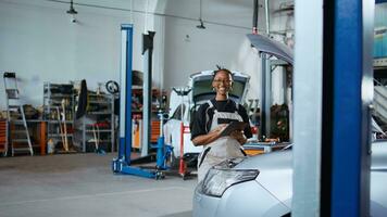 portret van vrolijk ingenieur werken in professioneel garage, gebruik makend van tablet naar beoordelen auto prestatie voordat maken vereist upgrades. blij reparatie winkel arbeider afstemmen omhoog voertuig foto