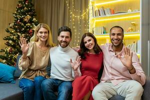 portret van nieuw jaar partij met verschillend vrienden Aan kerstmis, gasten op zoek Bij camera en golvend groet en lachend, zittend Aan sofa in de buurt Kerstmis boom in leven kamer. foto