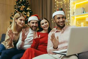 verschillend vrienden vieren nieuw jaar en Kerstmis samen huis, Kerstmis partij met gasten, mannen en Dames glimlachen en gelukkig samen pratend Aan video telefoontje groet vrienden van een afstand, gebruik makend van laptop. foto