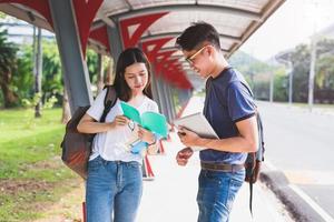 twee aziatische jonge universiteitsmensen die discussiëren over het lezen van een boek en het gebruik van een laptop voor het zoeken en leren van kennis. onderwijs en vriendschap concept. geluk en leerconcept. liefhebbers en vriend thema foto