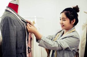 Aziatische vrouwelijke modeontwerper meisje passen op de formele pak uniforme kleding op mannequin model. modeontwerper stijlvolle showroom. naai- en kleermakersconcept. creatieve naaister stylist foto