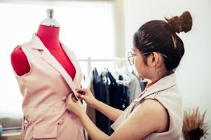 Aziatische vrouwelijke modeontwerper meisje passen op de formele kleding uniforme kleding op mannequin model. modeontwerper stijlvolle showroom. naai- en kleermakersconcept. creatieve naaister stylist foto