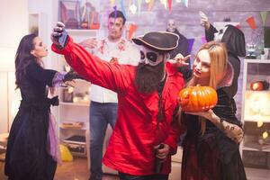 mooi vampier vrouw en haar pompoen nemen een selfie met gebaard piraat vieren halloween. foto