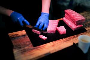 selectief focus Aan de handen van chef snijdend de vlees van tonijn Aan de snijdend bord foto