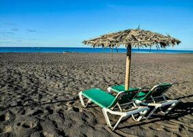 twee lounge stoelen en een paraplu Aan een zanderig strand foto