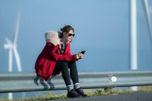 Aan de achtergrond van windmolens, een jong vrouw in een rood jasje is genieten van haar winter vakantie. foto