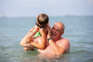 gelukkig opa en kleinzoon zijn spelen in de zee water.vader en zoon zijn resting Aan de zee. foto